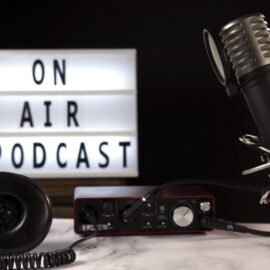Micrófono y equipo de grabación de podcast en estudio con cartel luminoso “On Air Podcast”